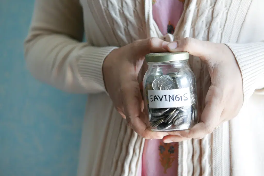 Woman holding a jar filled with coins that says Savings.