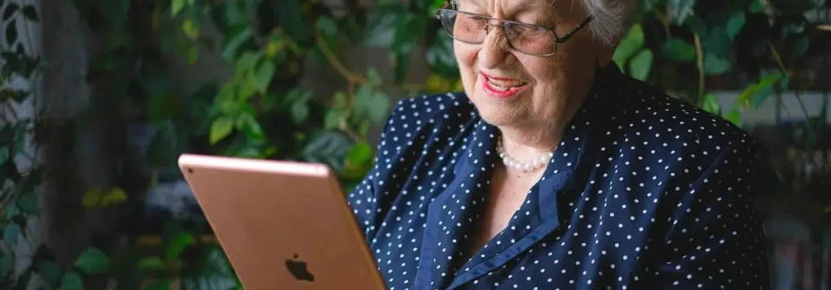 Old woman using a tablet with leaves behind her.