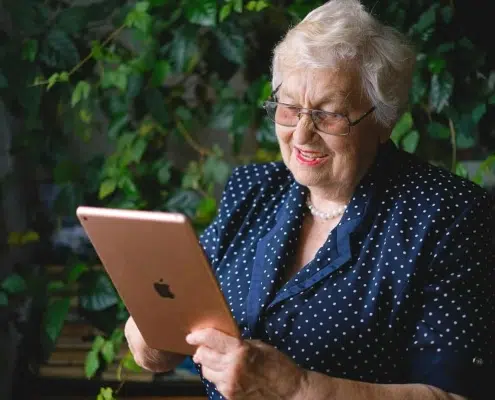 Old woman using a tablet with leaves behind her.