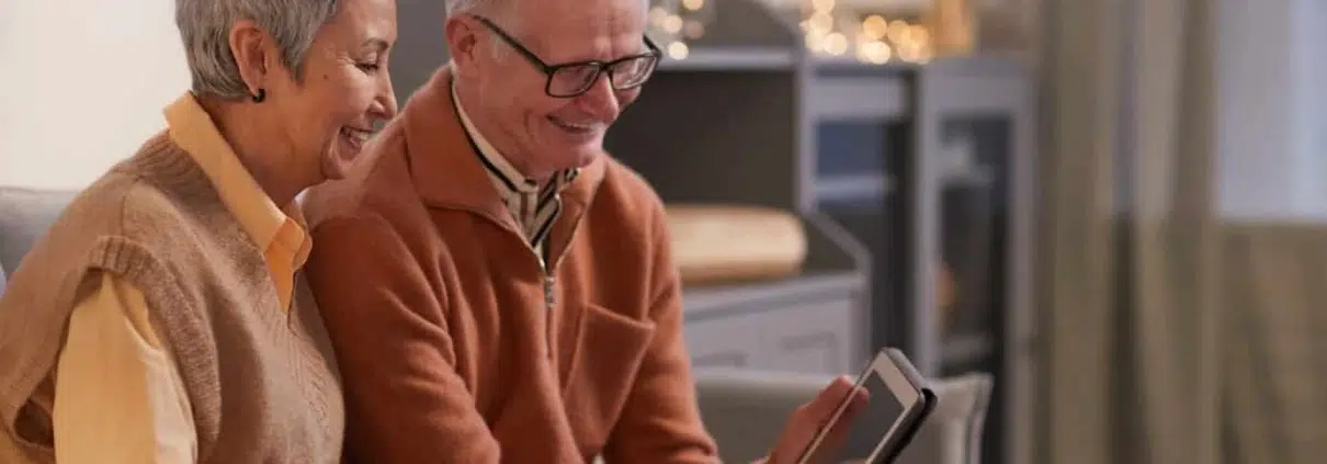 Old couple using a tablet while sitting on a couch.