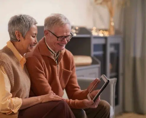 Old couple using a tablet while sitting on a couch.