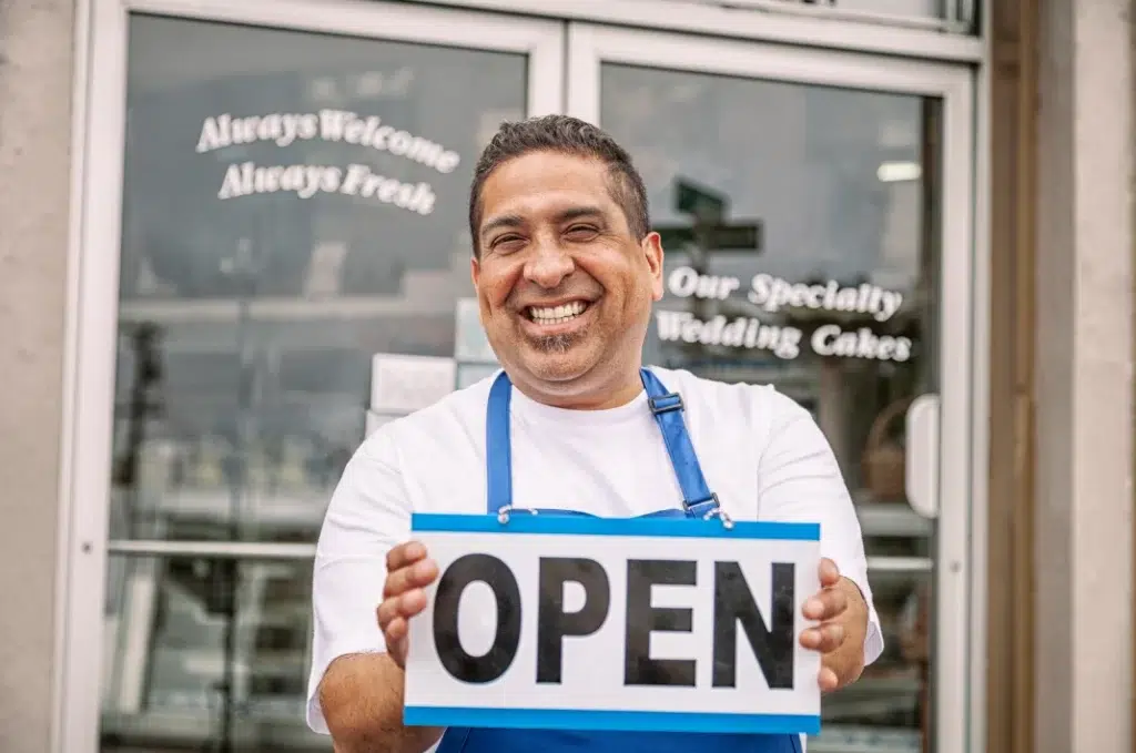 A man carrying a signage that says open in front of his business store.
