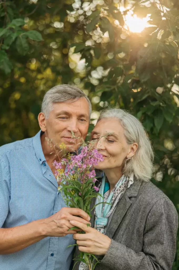An elderly couple smelling a flower.