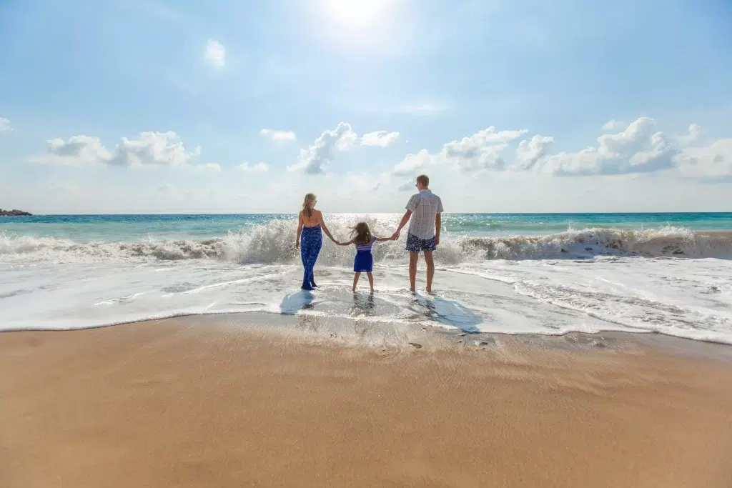Father, mother and little daughter holding hands on seashore.