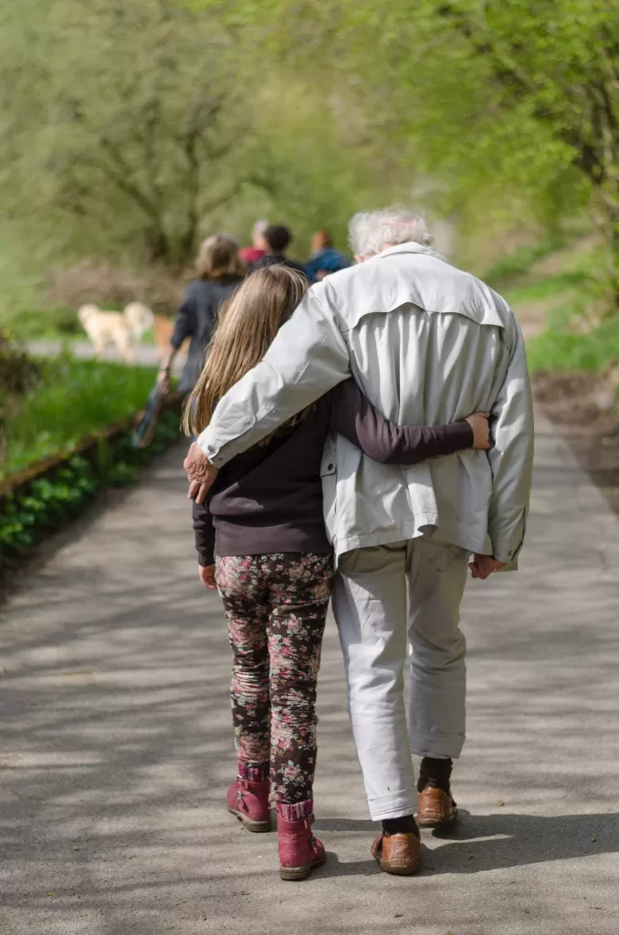 Grandfather and granddaughter hugging each other while walking.