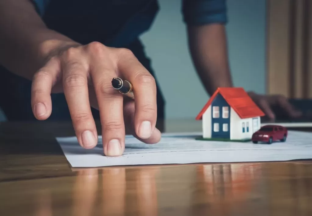Hand holding a pen with miniature cars and house.