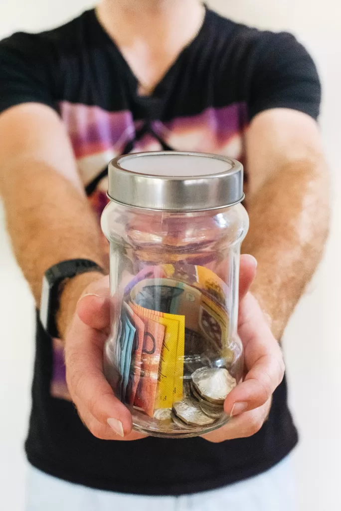 Man holding clear glass jar filled with Australian money.