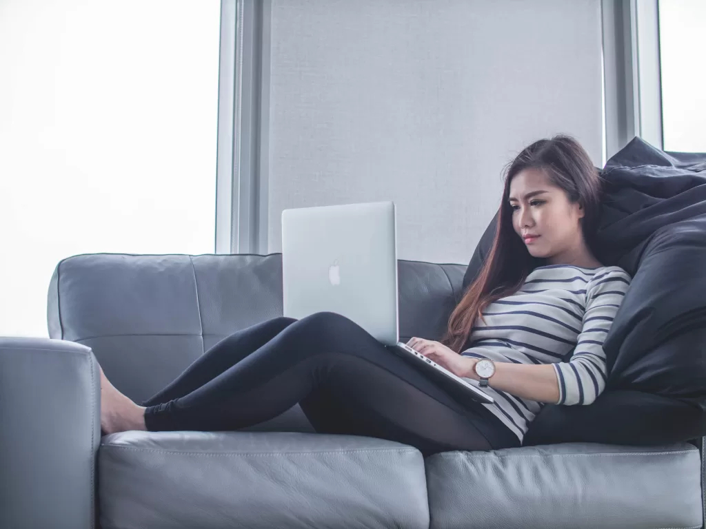 Woman sitting on sofa while using a laptop.