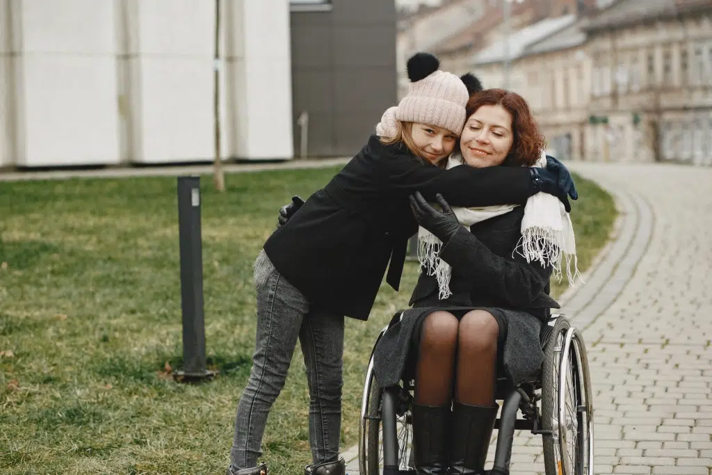 A little girl hugging a woman in a wheelchair.