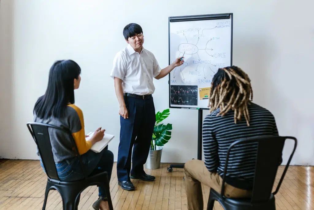 Man explaining his colleagues about cryptocurrency on a white board.