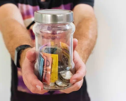 Man holding a transparent jar filled with paper money and coins.