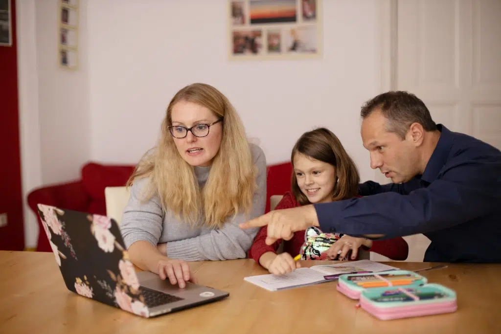 Parents teaching their child while looking at the laptop.