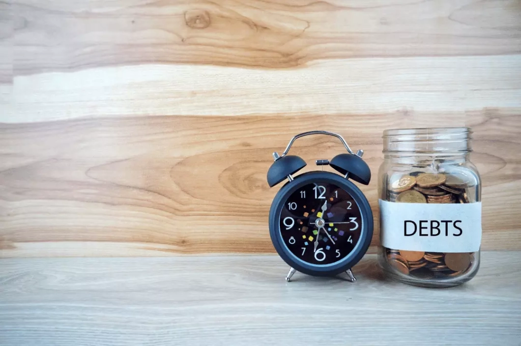 Debt jar with coins and alarm clock.