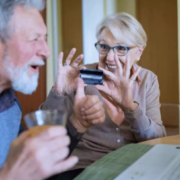 Elderly man happy on computer wife holds credit card.
