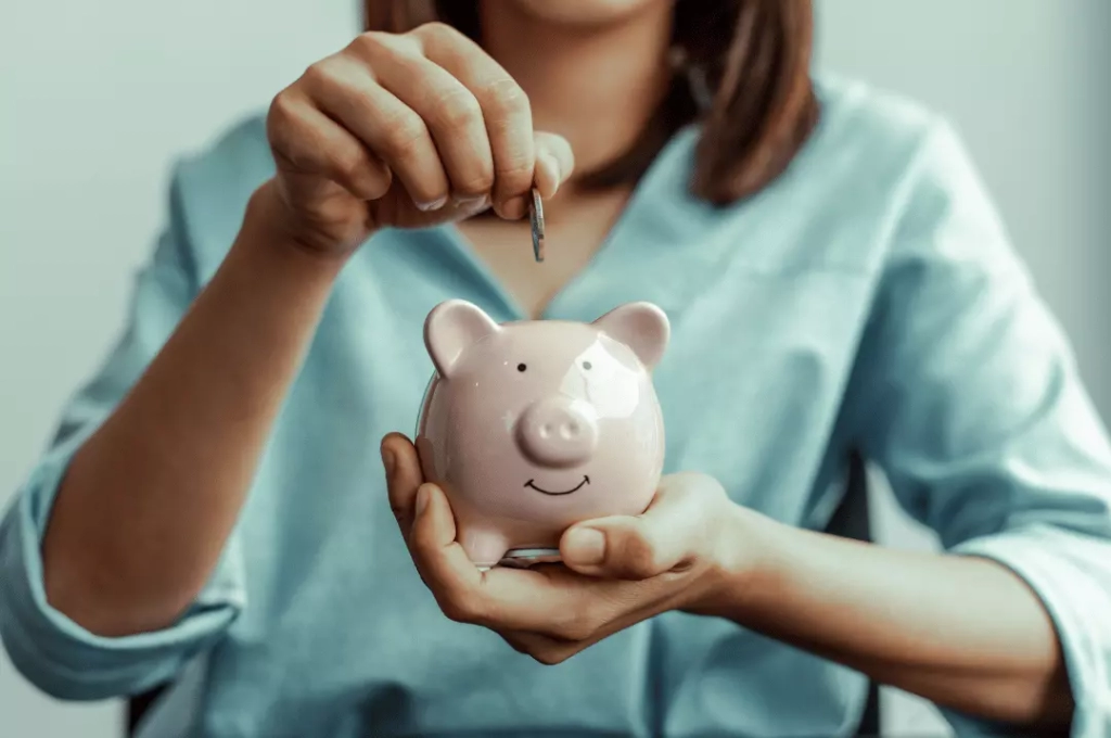 Woman inserting coin in piggy bank.