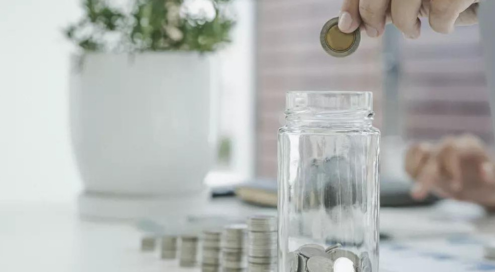 Adding coin to jar with stacked coins in background.