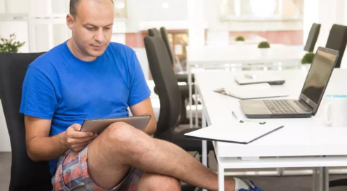 Casual employee using a tablet while wearing shorts in the office.