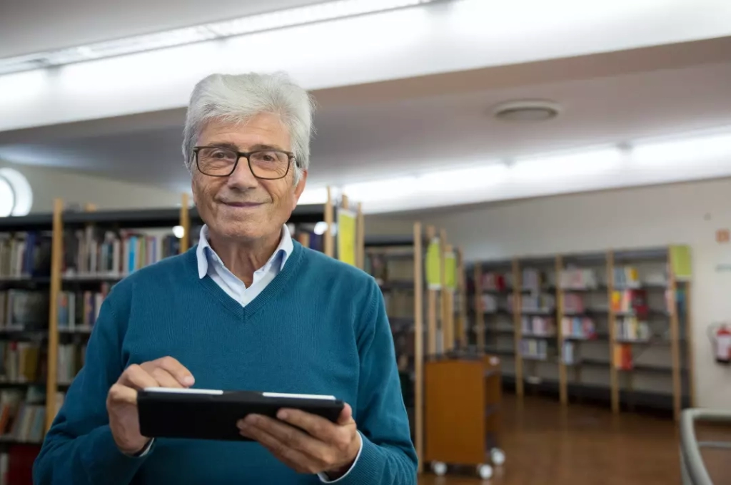 Old man using a tablet in the library.