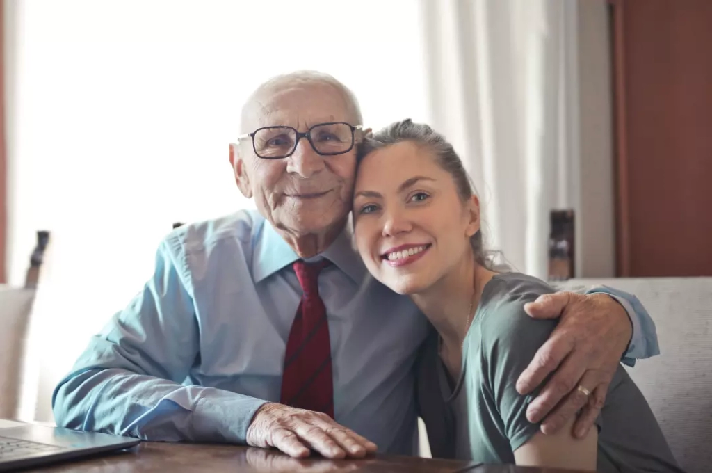 An elderly man embraces a woman at a table, pondering retirement and the possibility of returning to work.