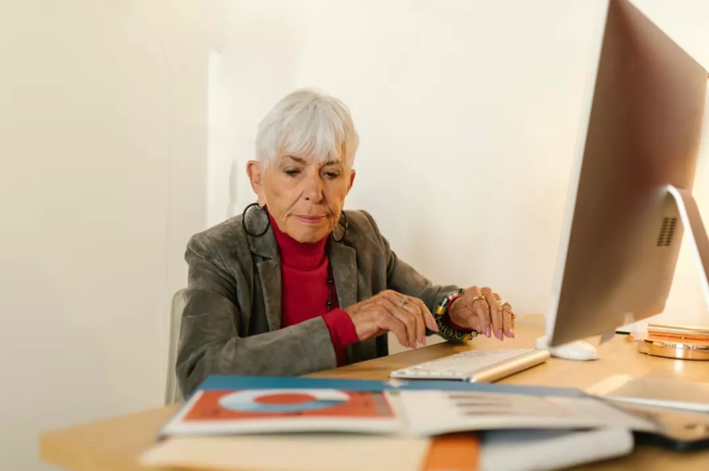 An older woman balancing retirement and work by using a computer at home.