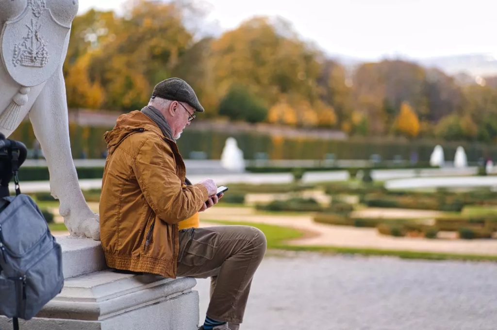 A self-funded retiree sitting on a bench while looking at his phone.