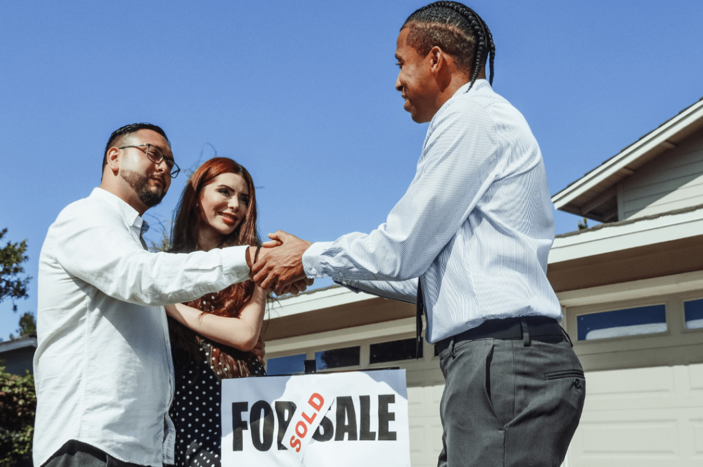 Couple shaking hands with a realtor after buying their first home.