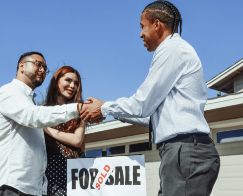 Couple shaking hands with a realtor after buying their first home.