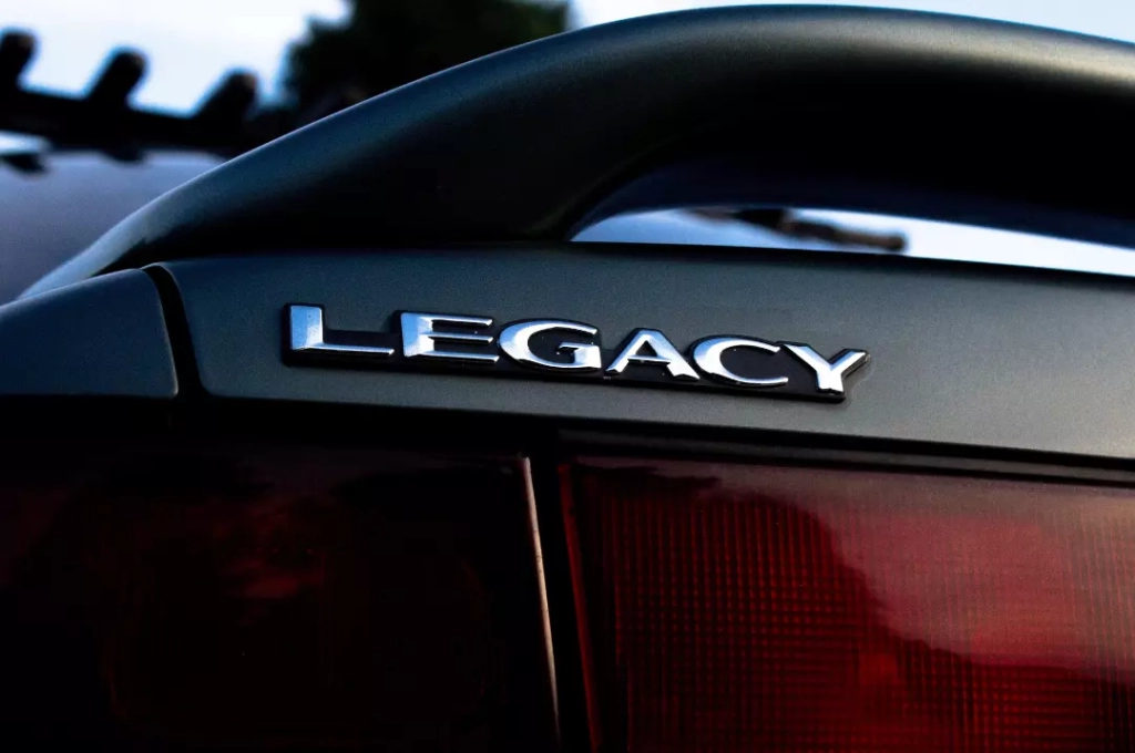 The word legacy at the back of the black and red car.