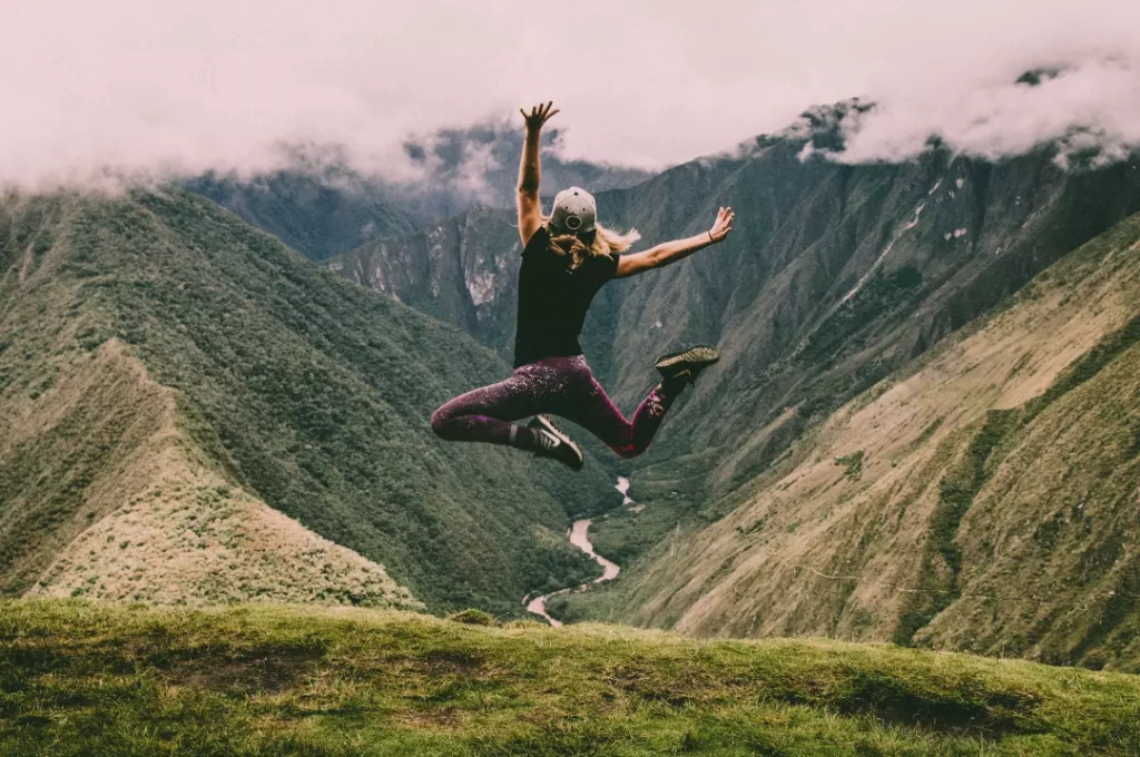 Happy woman jumping on green mountains.