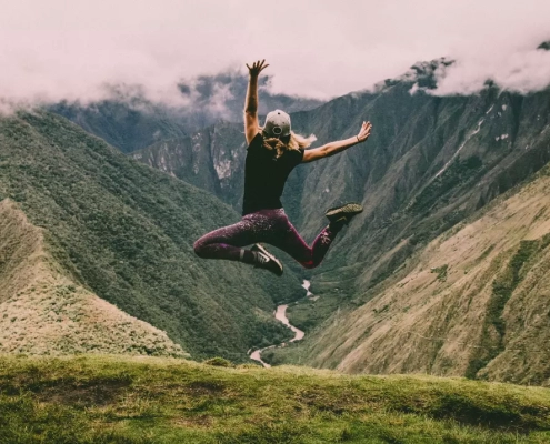 Happy woman jumping on green mountains.