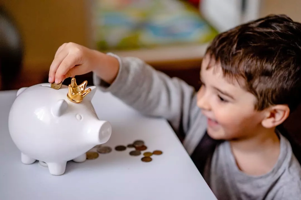 Little boy saving coins in his piggy bank.